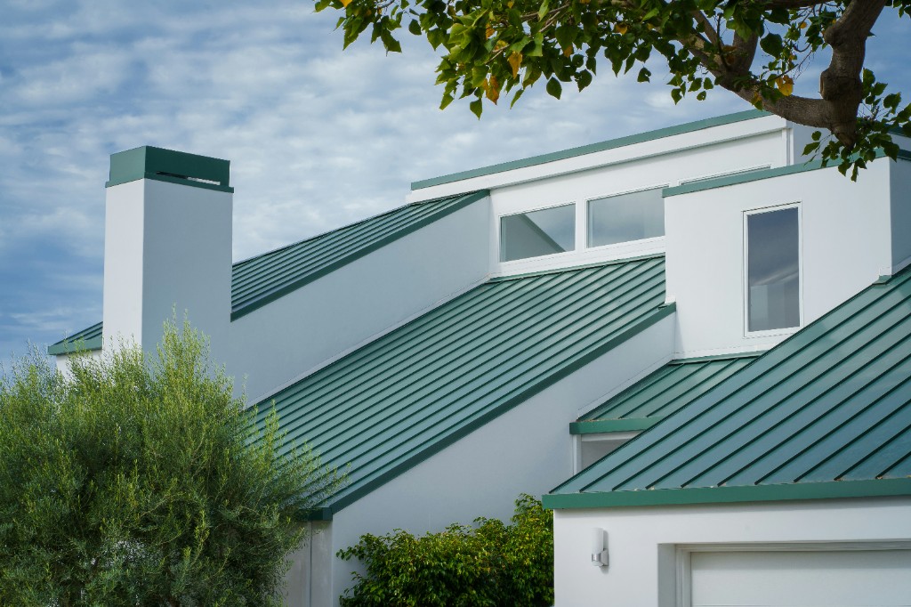 White home with a standing-seam green metal roof against a blue sky