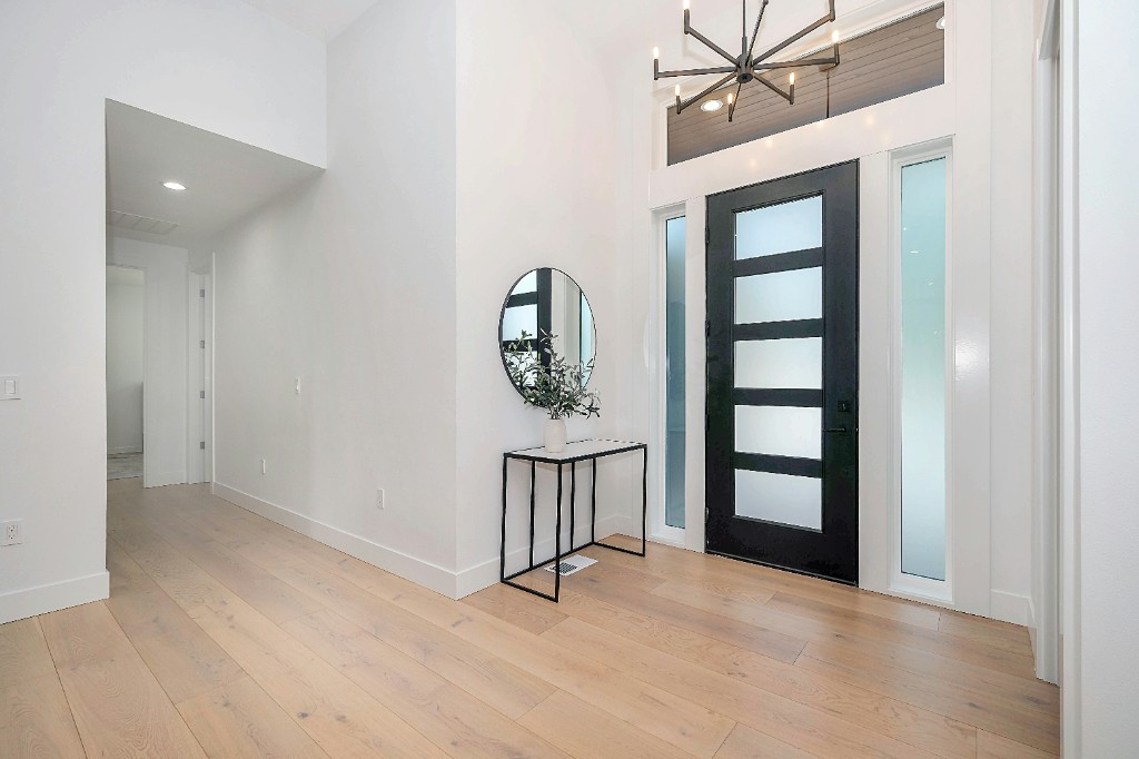 Modern black glass-panel front door in a bright entryway with hardwood floors