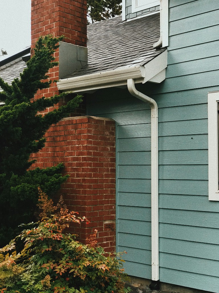 White seamless gutters and downspout on a blue-sided home with a brick chimney