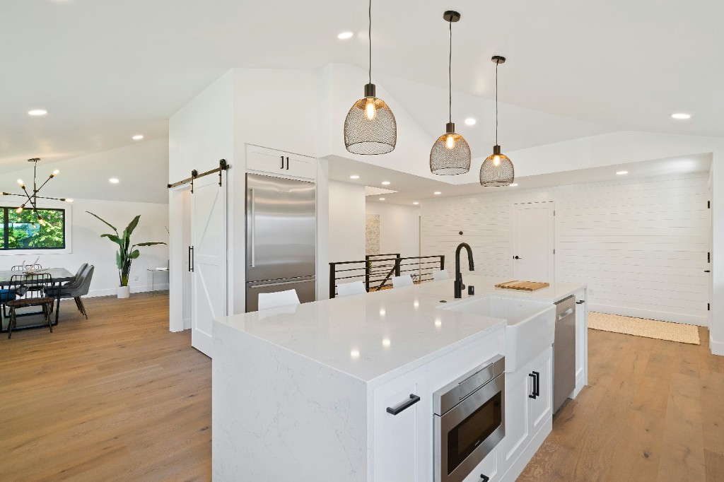 Remodeled kitchen with a large marble waterfall island, white cabinets, and pendant lighting
