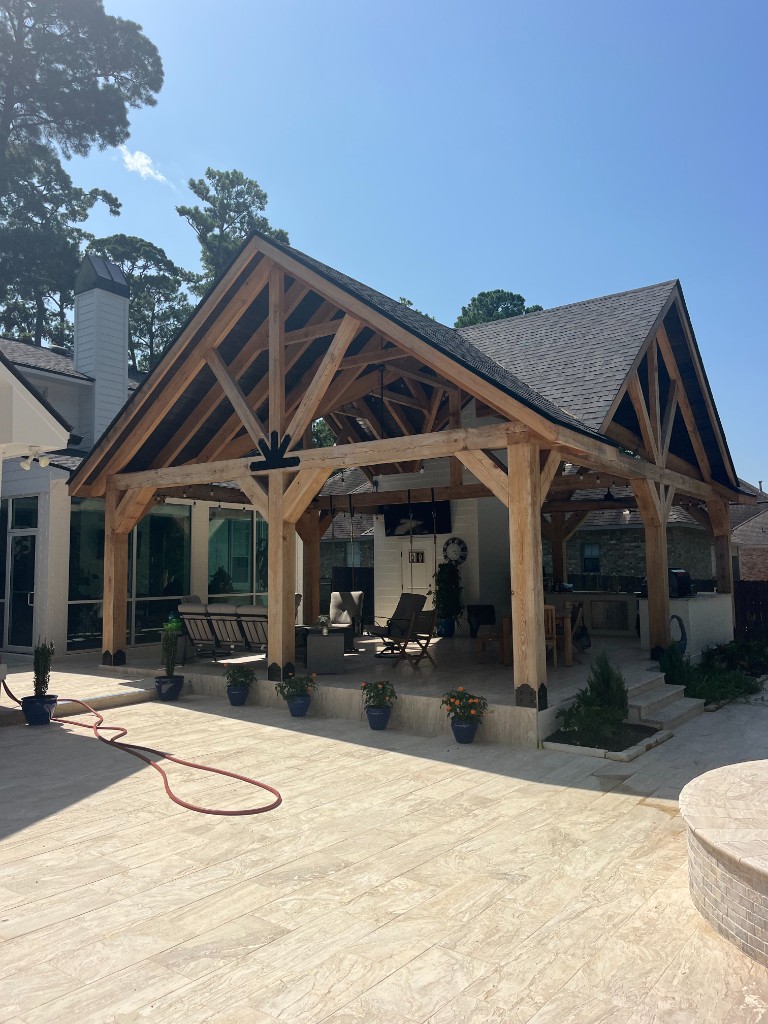 Covered outdoor kitchen pavilion with timber framing, a built-in grill, and a travertine patio